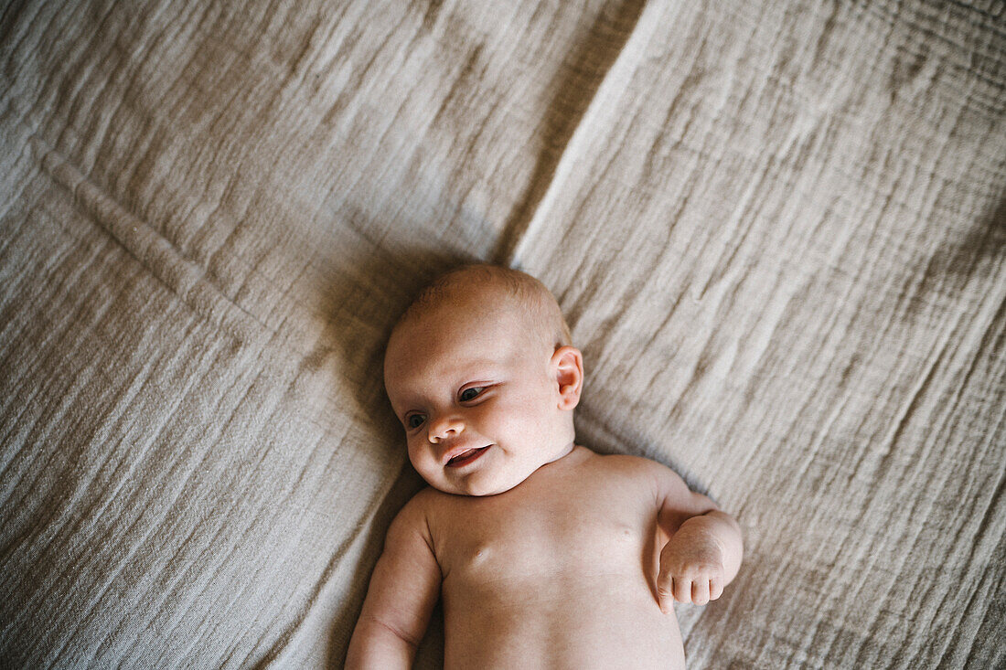 Neugeborenes Baby ohne Hemd auf dem Bett liegend