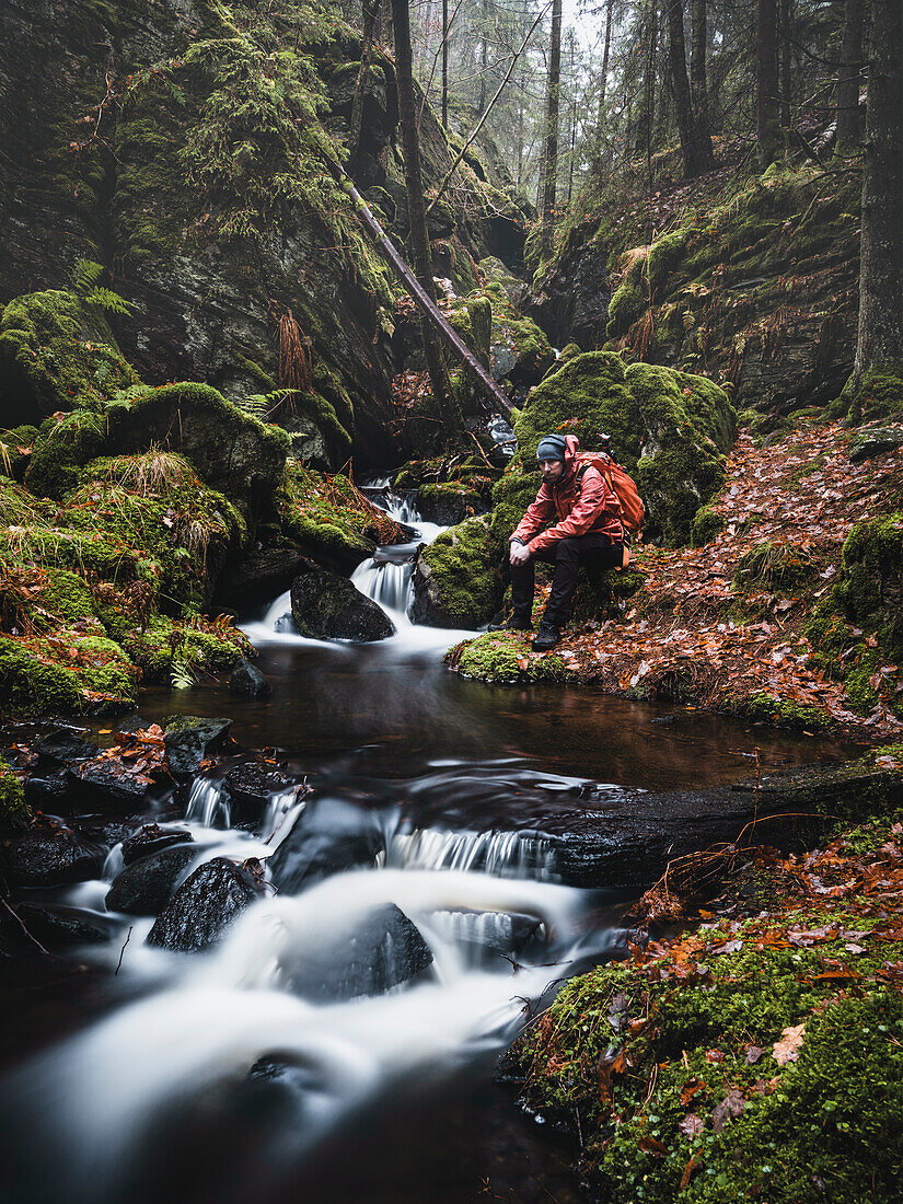 Wanderer sitzt am Bach im Wald
