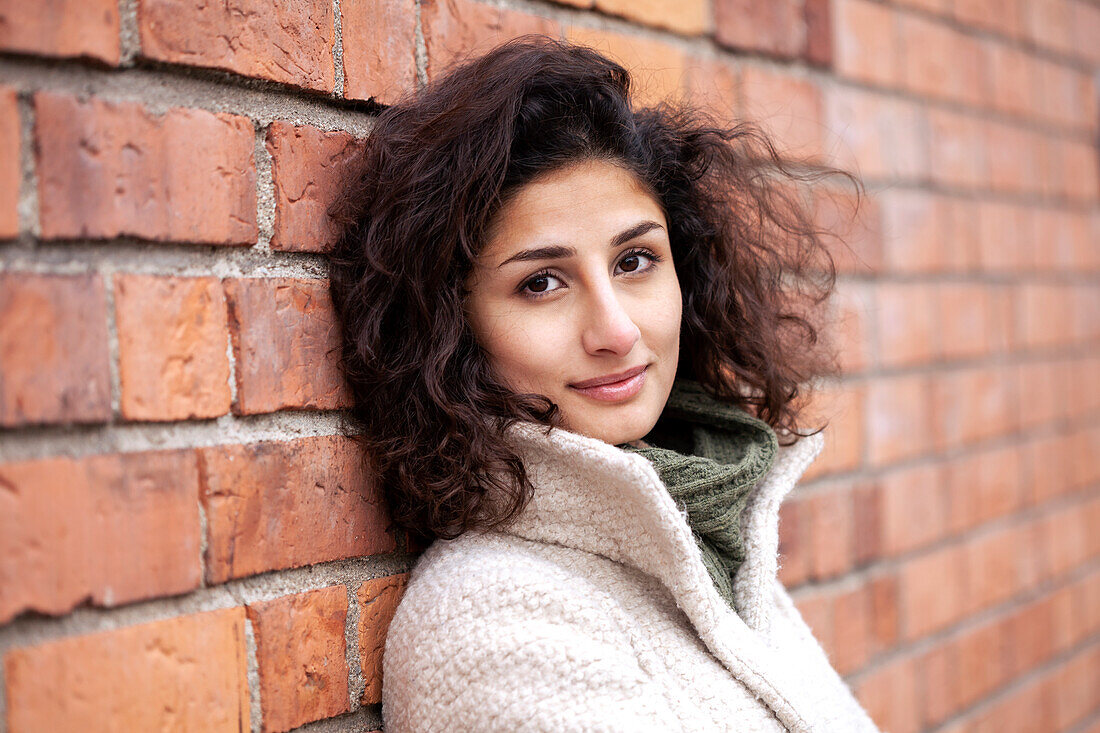 Portrait of young woman leaning against brick wall