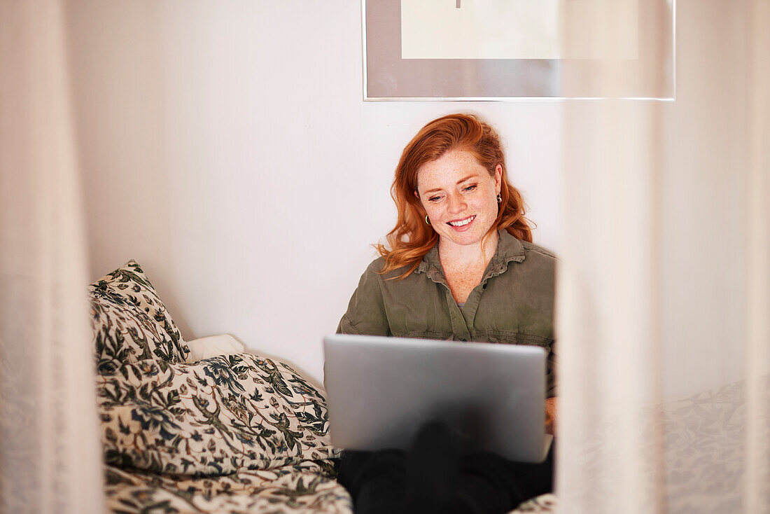 Lächelnde Frau mit Laptop auf dem Bett