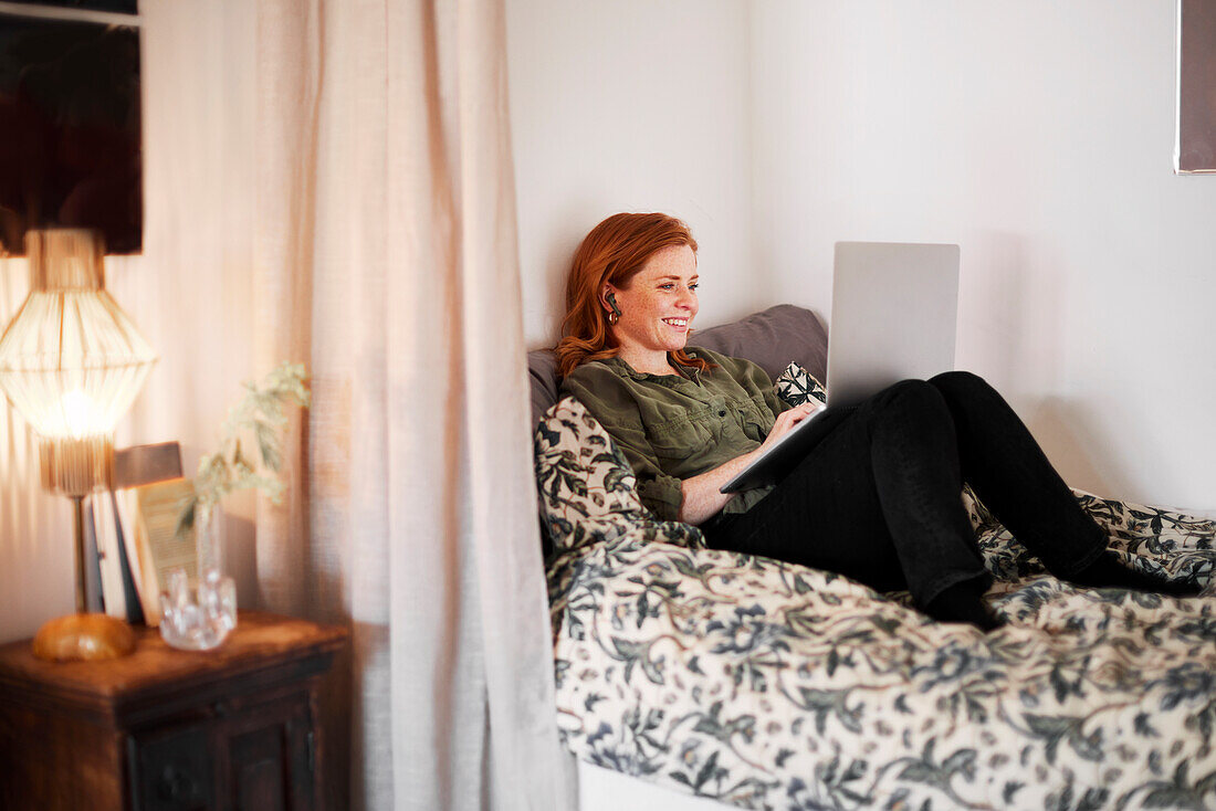 Smiling woman using laptop on bed