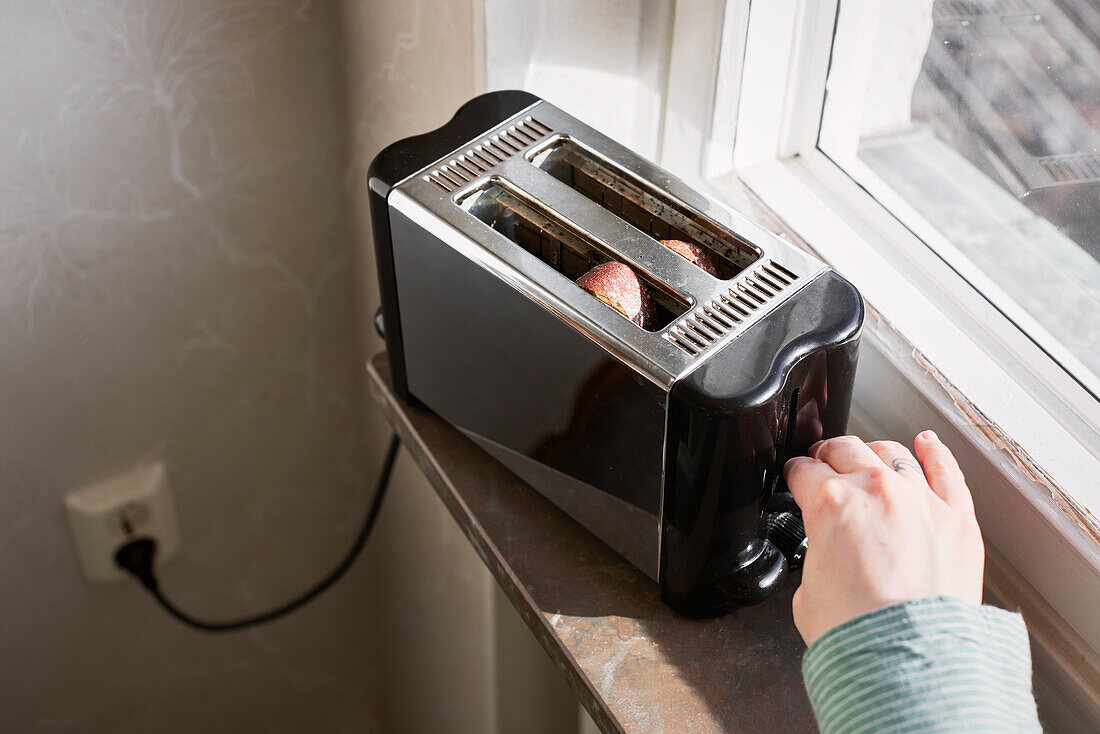 Hände stecken Toasts in den Toaster