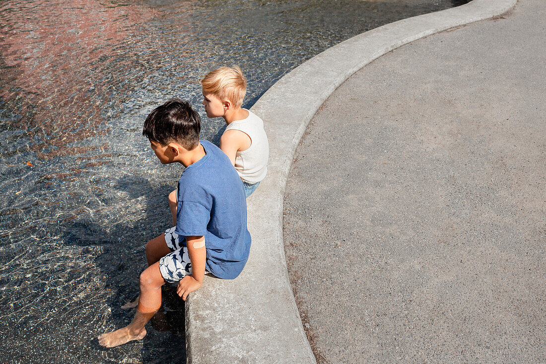 Kinderfreunde sitzen mit den Füßen im Teich