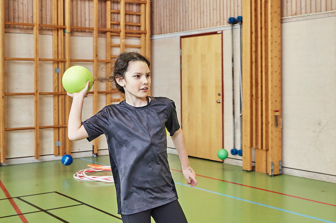 Mädchen wirft Ball im Sportunterricht in der Turnhalle der Schule