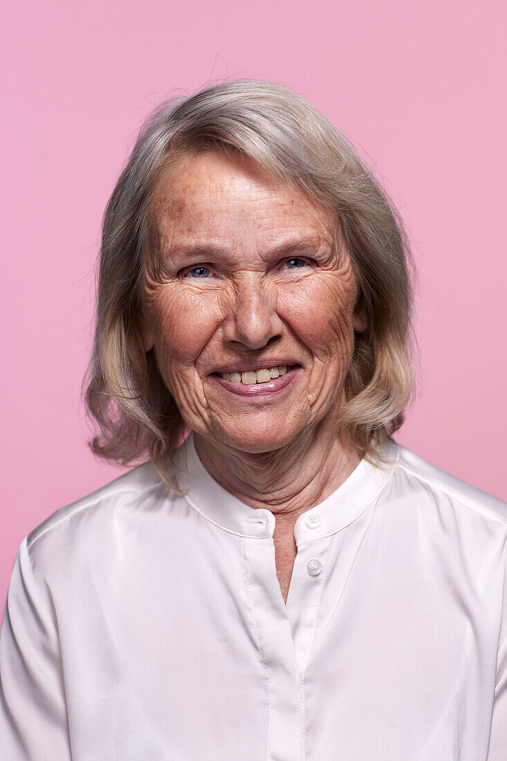 Portrait of smiling senior woman against pink background