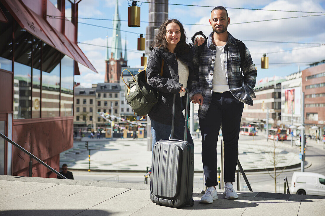 Portrait of smiling man and woman with luggage in city center