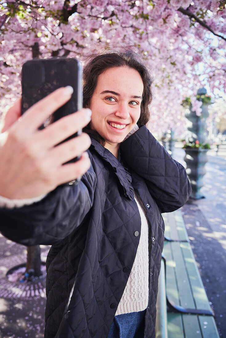 Junge Frau macht ein Selfie vor Kirschbäumen