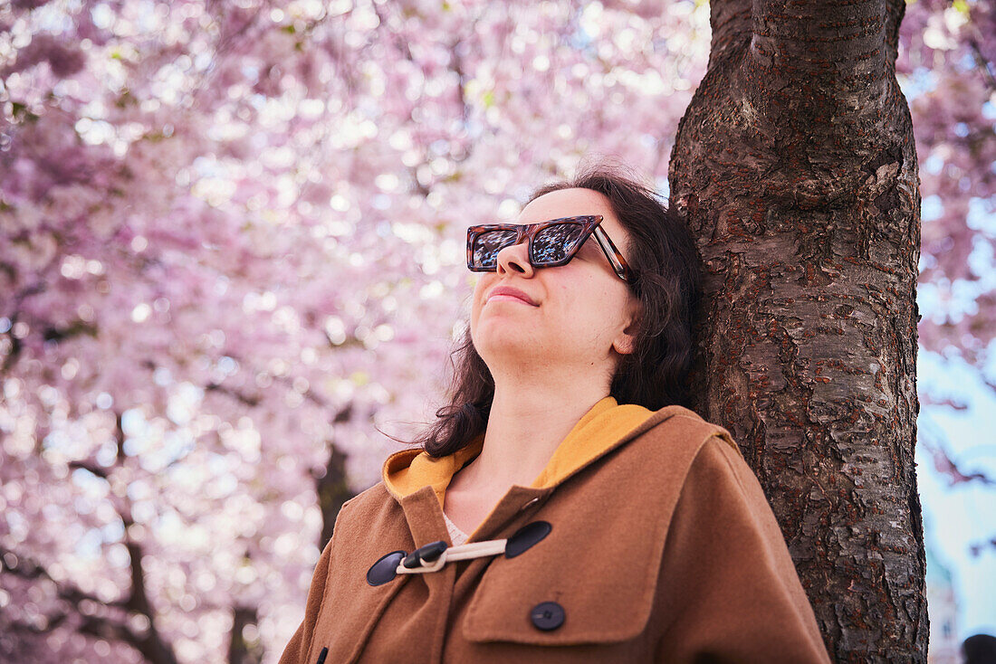 Junge Frau steht unter einer Kirschblüte