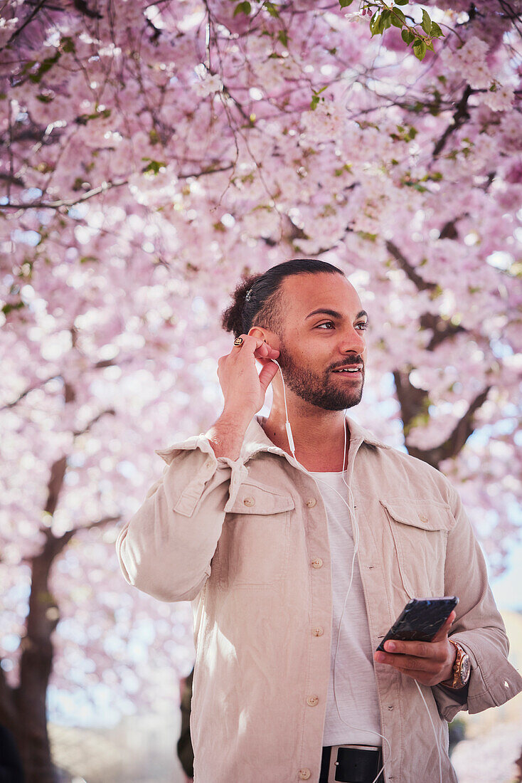 Young man standing under cherry blossom and using phone