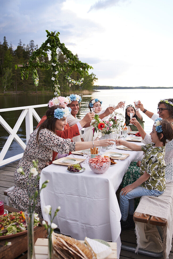 Family raising toast during midsummer dinner by lake