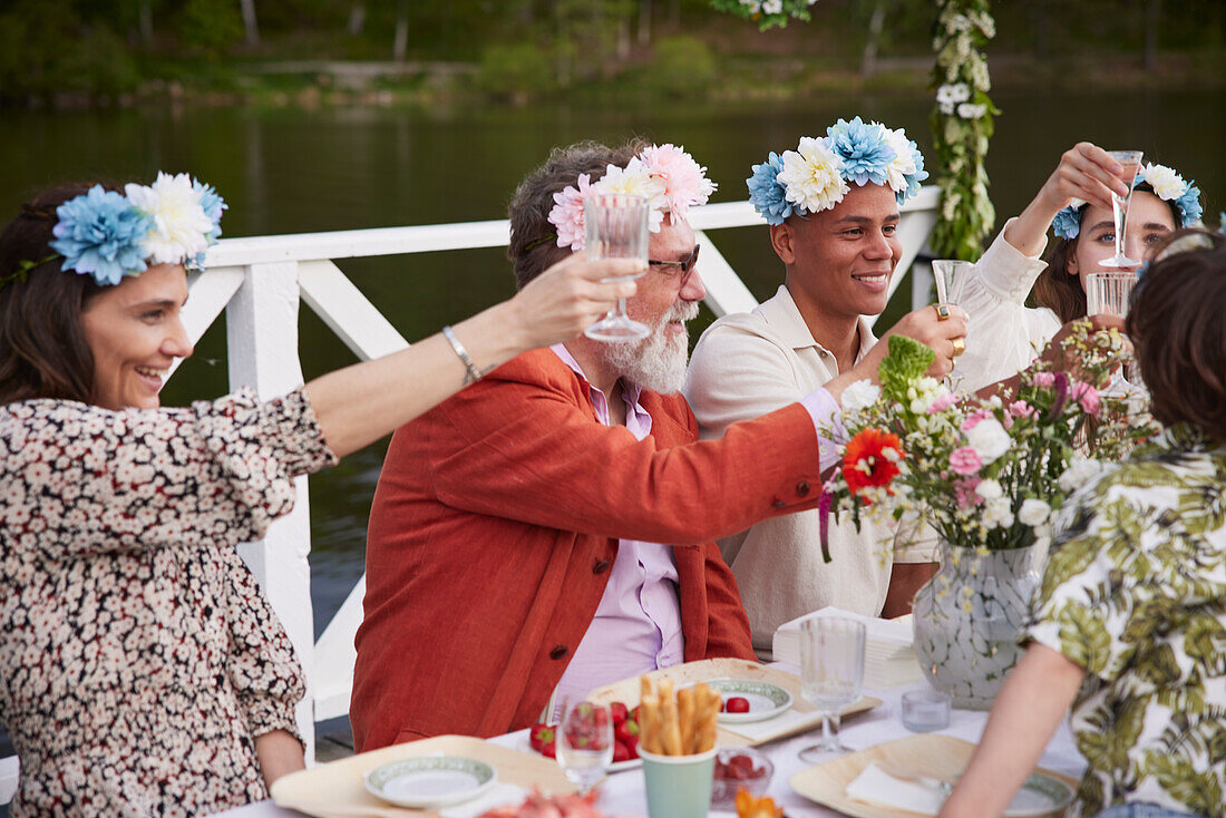 Family raising toast during midsummer dinner by lake