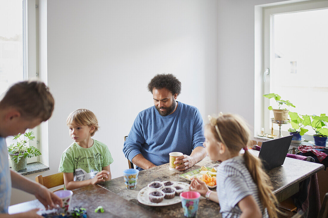Father with children sitting at table and having snack