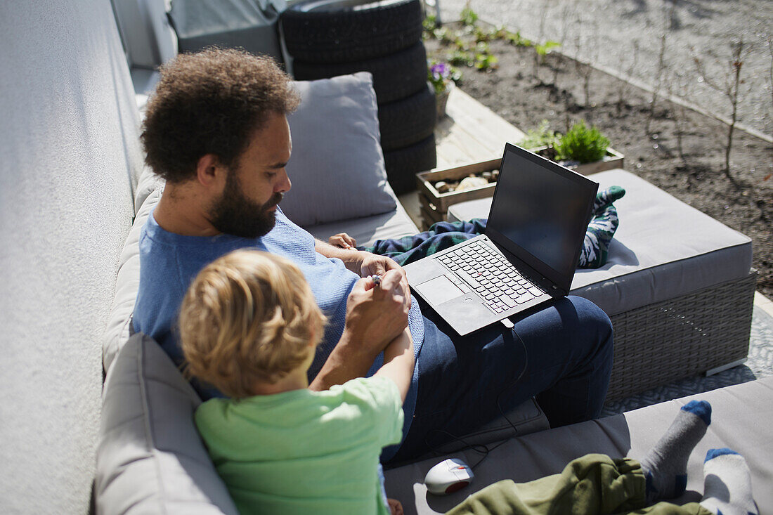 Vater sitzt mit Sohn an Deck und arbeitet am Laptop
