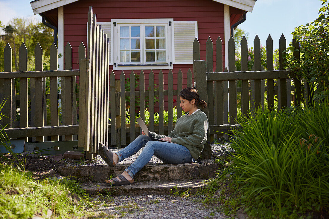 Woman with laptop in front of wooden house