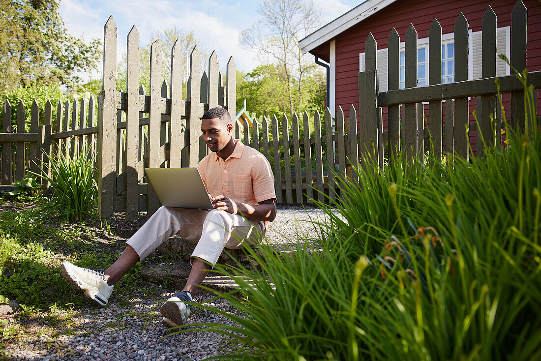 Man with laptop in front of wooden house