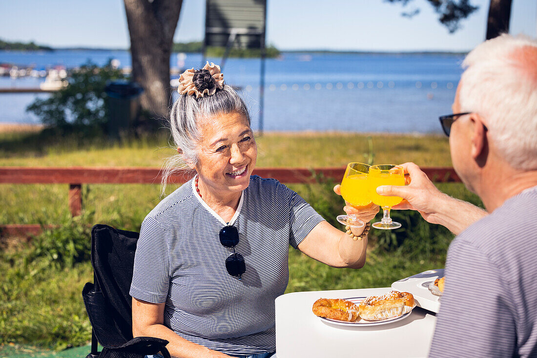 Senior couple having meal and rising toast at camp site