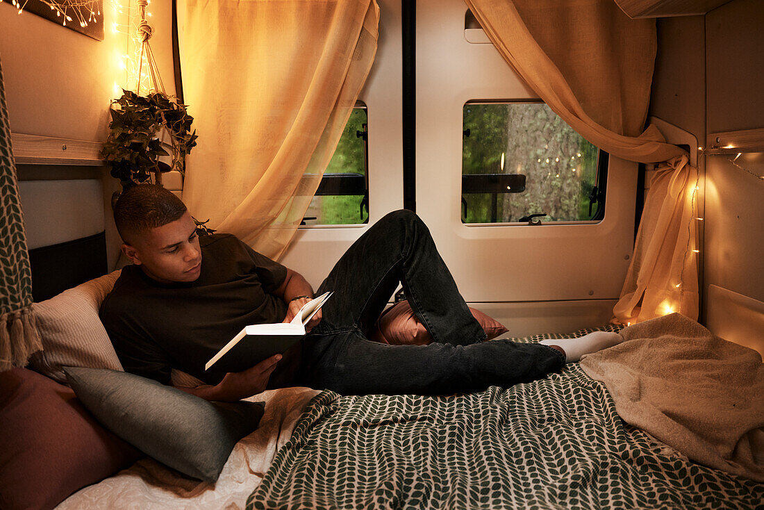 Mann liest ein Buch auf dem Bett im Wohnmobil