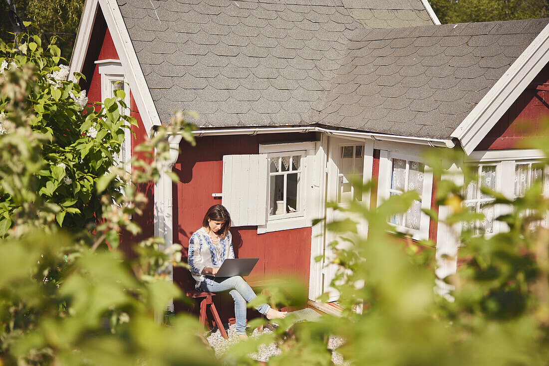 Woman using laptop in front of house