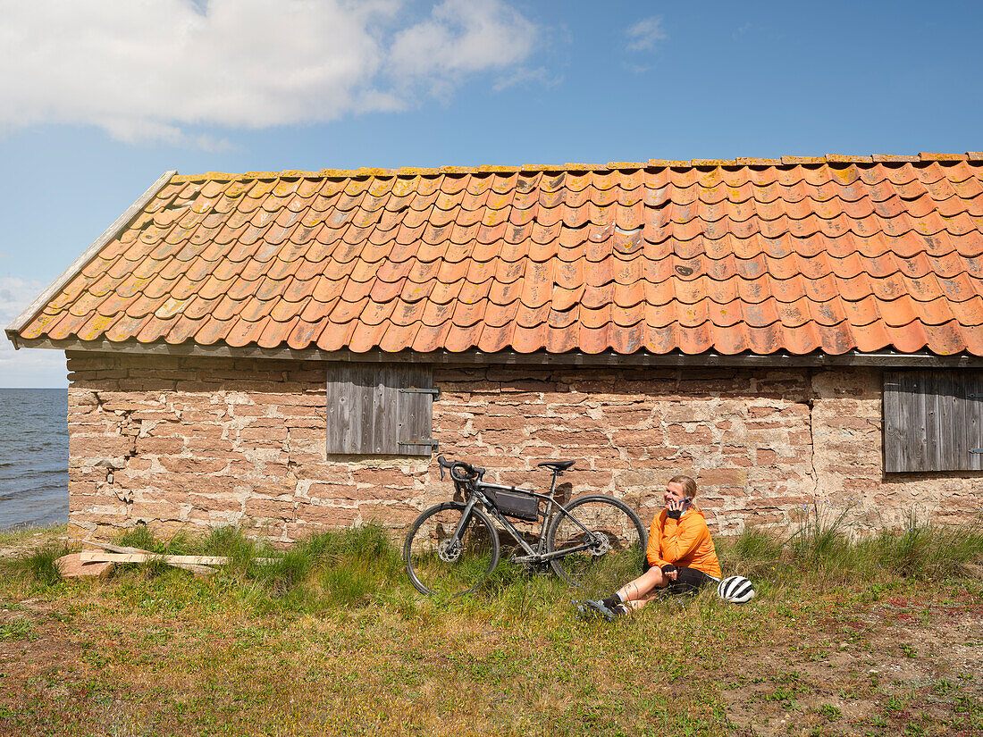 Cyclist relaxing near stone house at sea