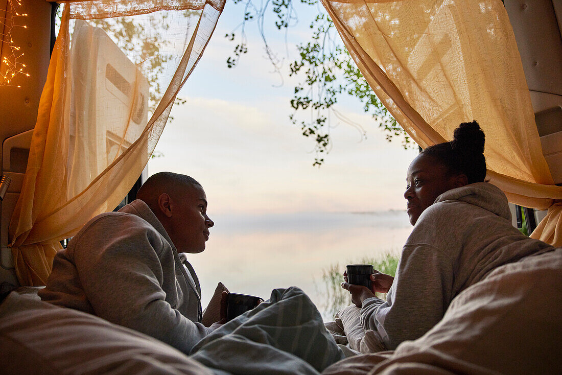 Young couple relaxing in camper van and looking at lake