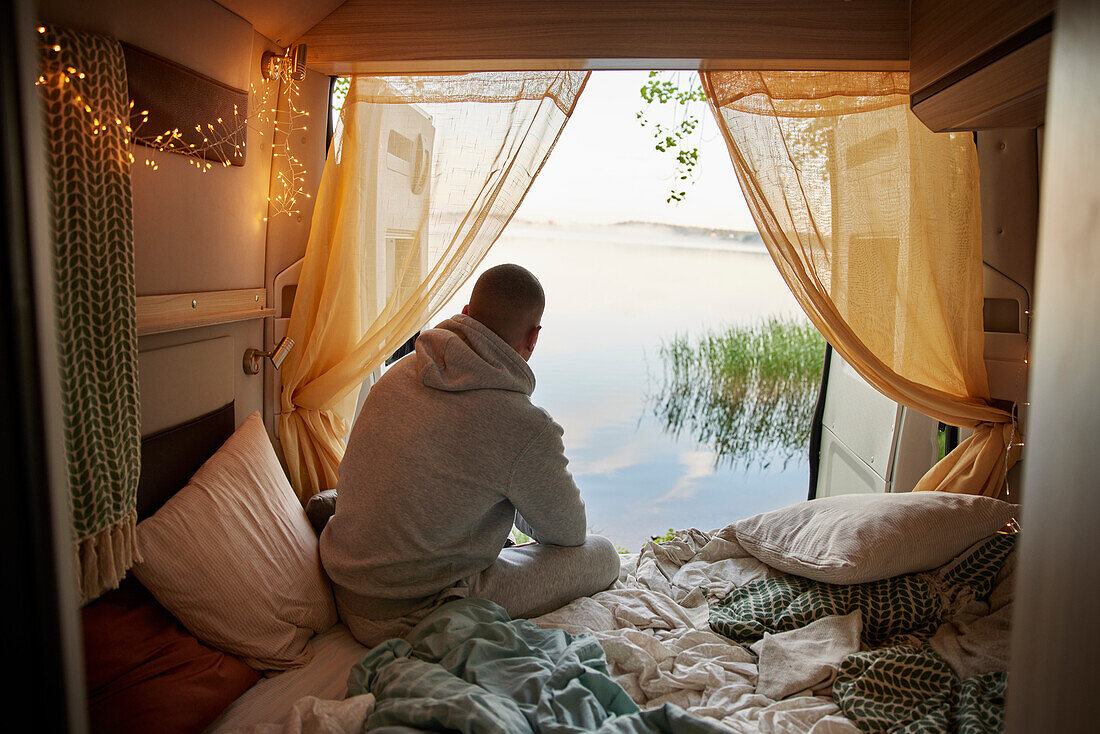 Mann sitzt im Wohnmobil und schaut auf den See