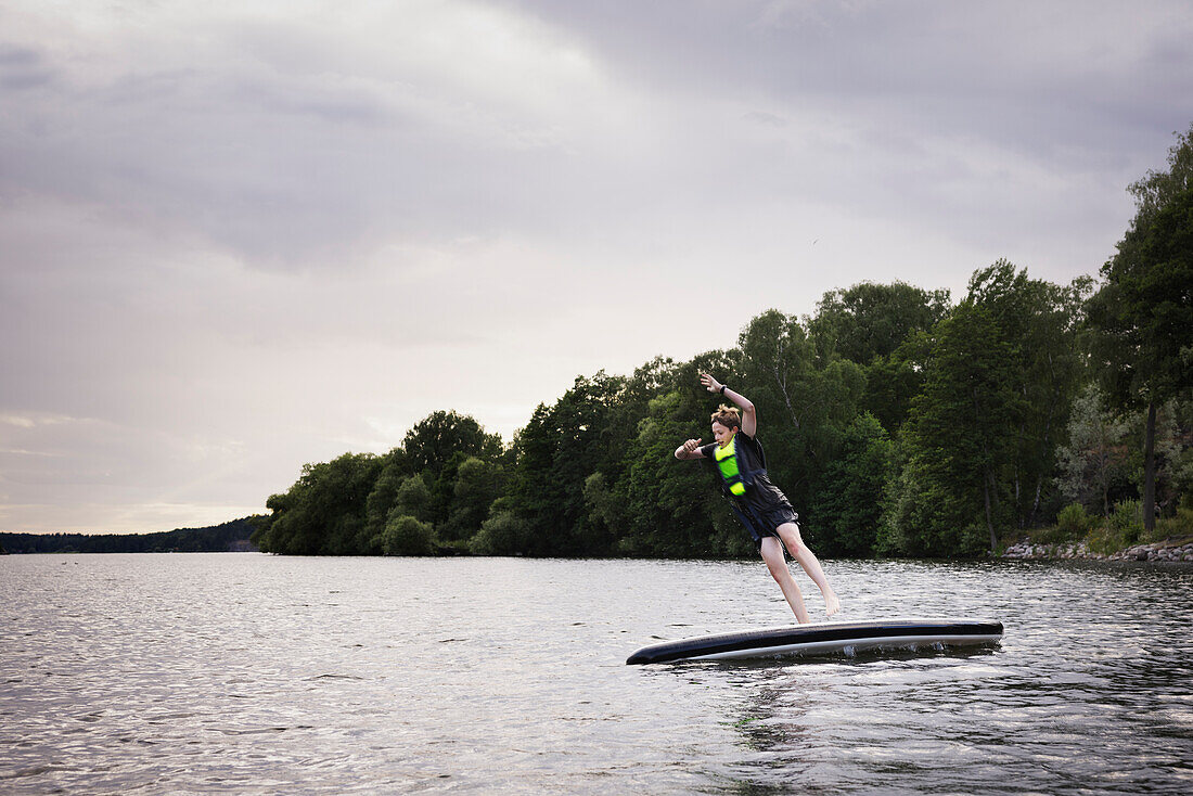 Boy jumping from paddle board on lake