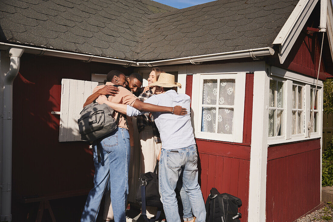 Lächelnde Freunde umarmen sich vor einem Holzhaus