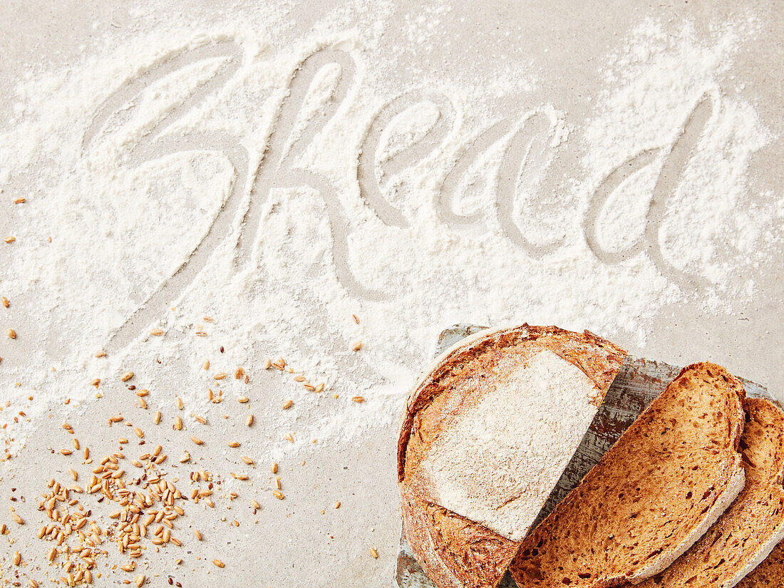 Angeschnittenes Brot, Getreidekörner und Schriftzug 'Bread' in Mehl