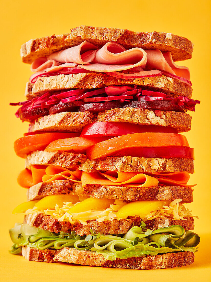 Riesiges Regenbogen-Sandwich vor gelbem Hintergrund