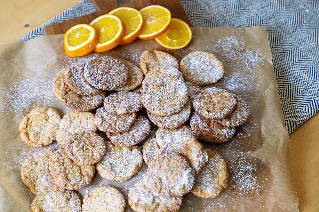 Orange cookies with powdered sugar and orange slices on parchment paper