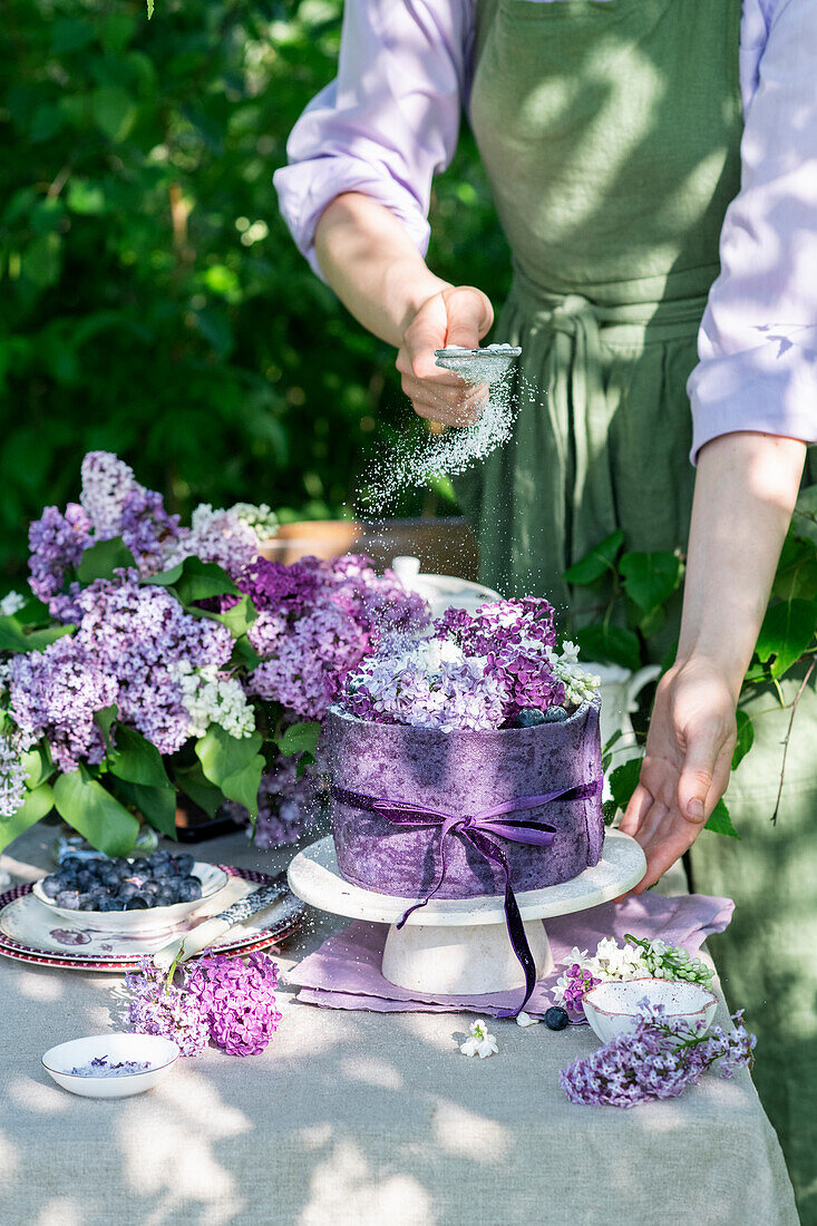 Heidelbeertorte gefüllt mit Profiteroles auf Gartentisch umgeben von Fliederblüten