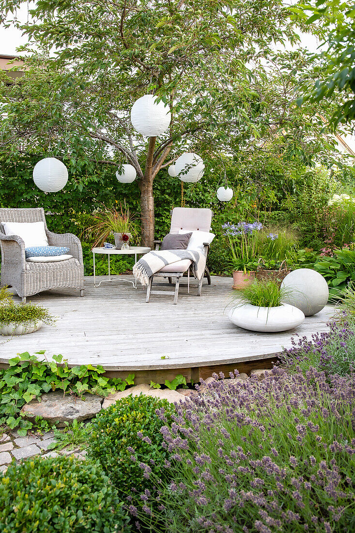 Round wooden terrace with seating under an ornamental cherry tree with white lanterns