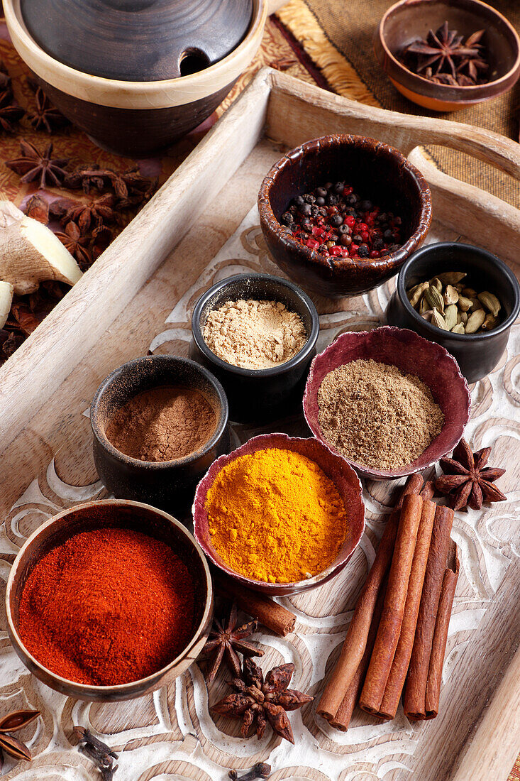 Various spices in small bowls on a wooden tray