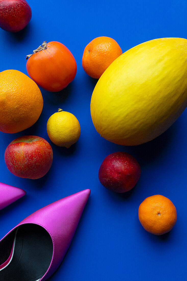Früchte und pinkfarbene Damenschuhe auf blauem Untergrund