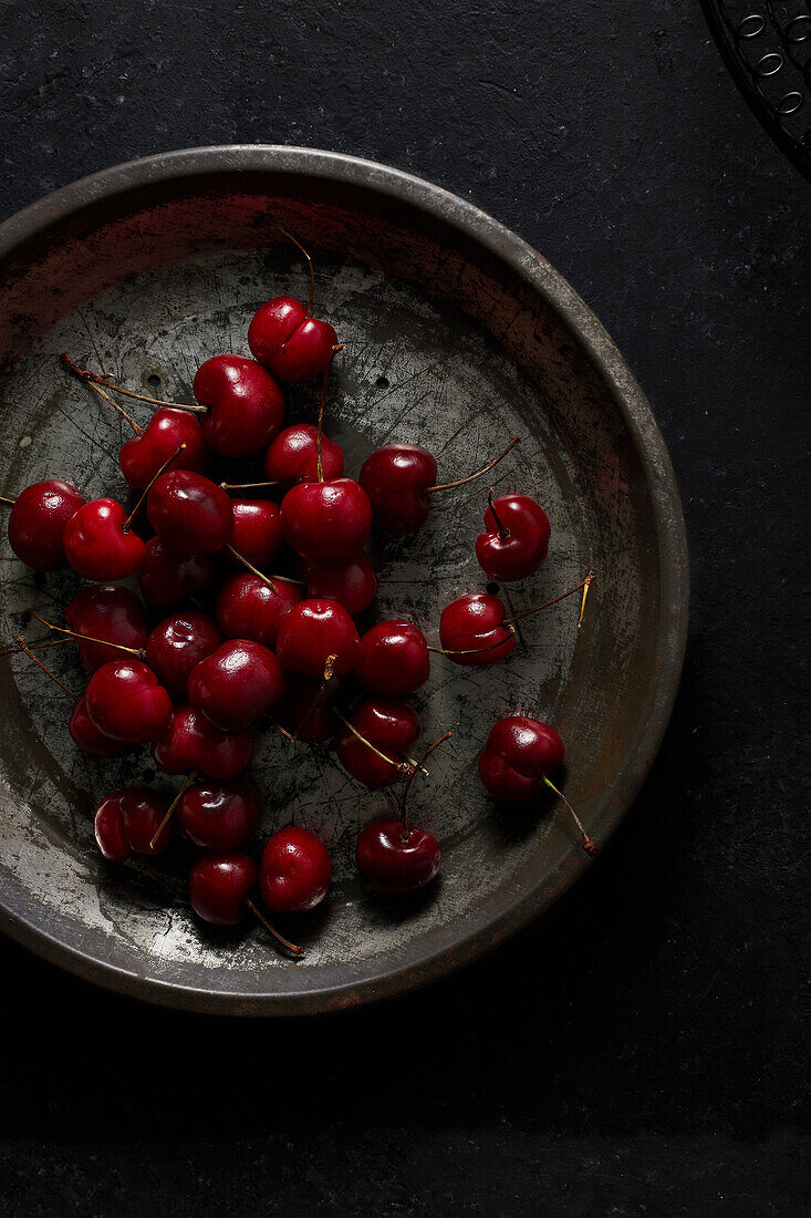 Fresh red cherries in a pie tin on a dark black surface
