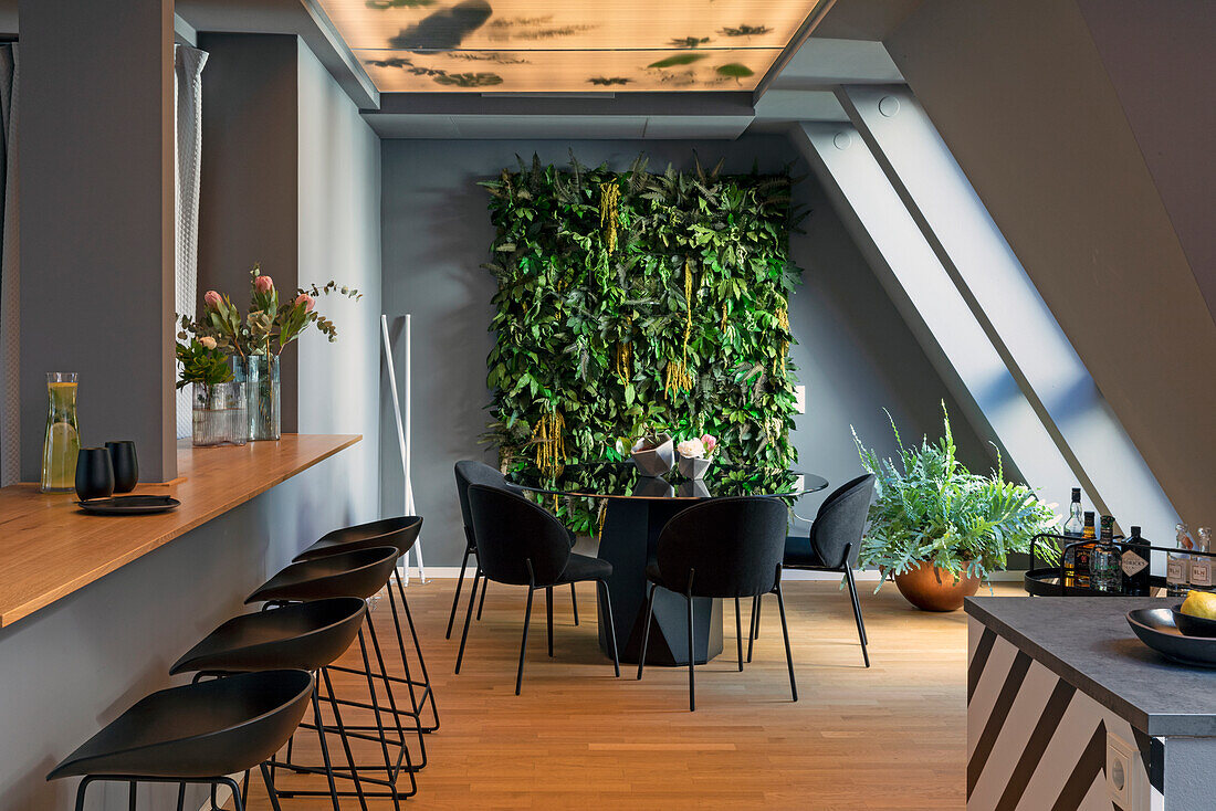 Long counter with black bar stools, small dining area and vertical garden in the background