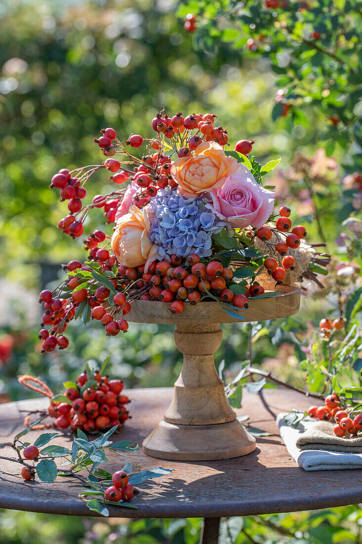 Herbstliches Blumenarrangement mit Rosen, Hortensien und Hagebutten auf Holzständer