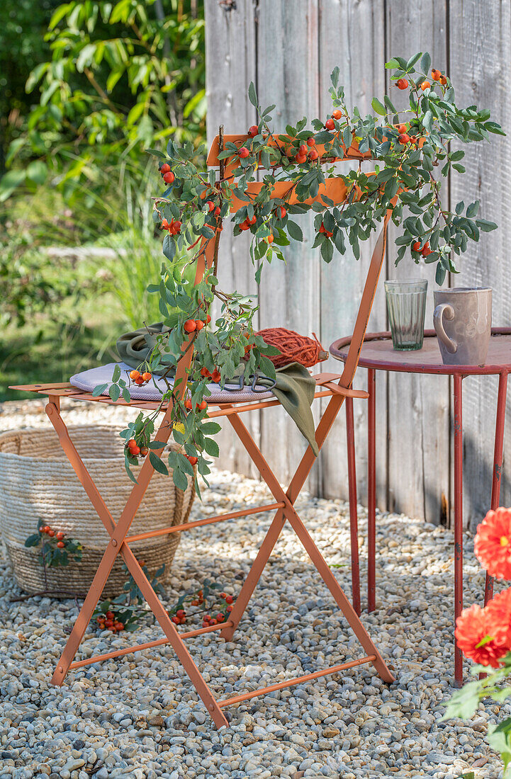 Orangefarbener Gartenstuhl farblich passend dekoriert mit Hagebuttenzweigen