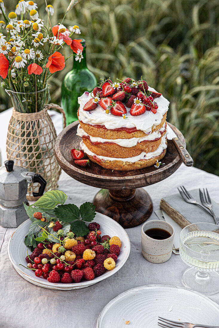 Gedeckter Tisch mit Kuchen, Blumenstrauß und Beeren im Freien