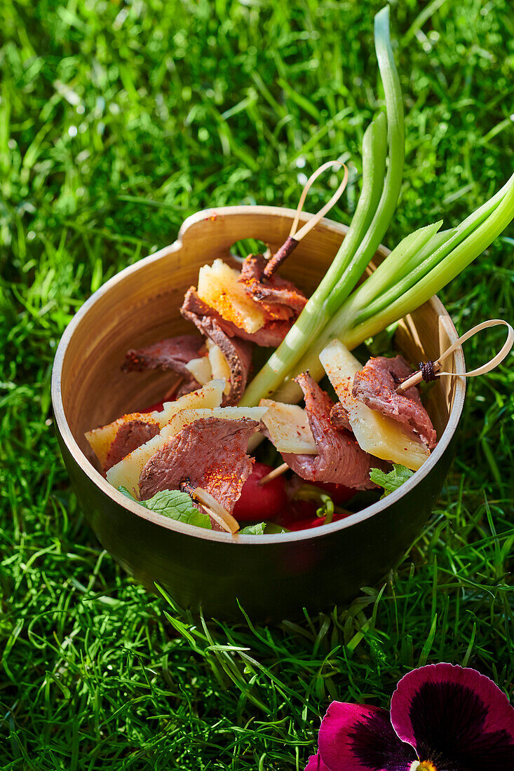 Spieße mit Entenbrust und Käse in Schale auf Wiese