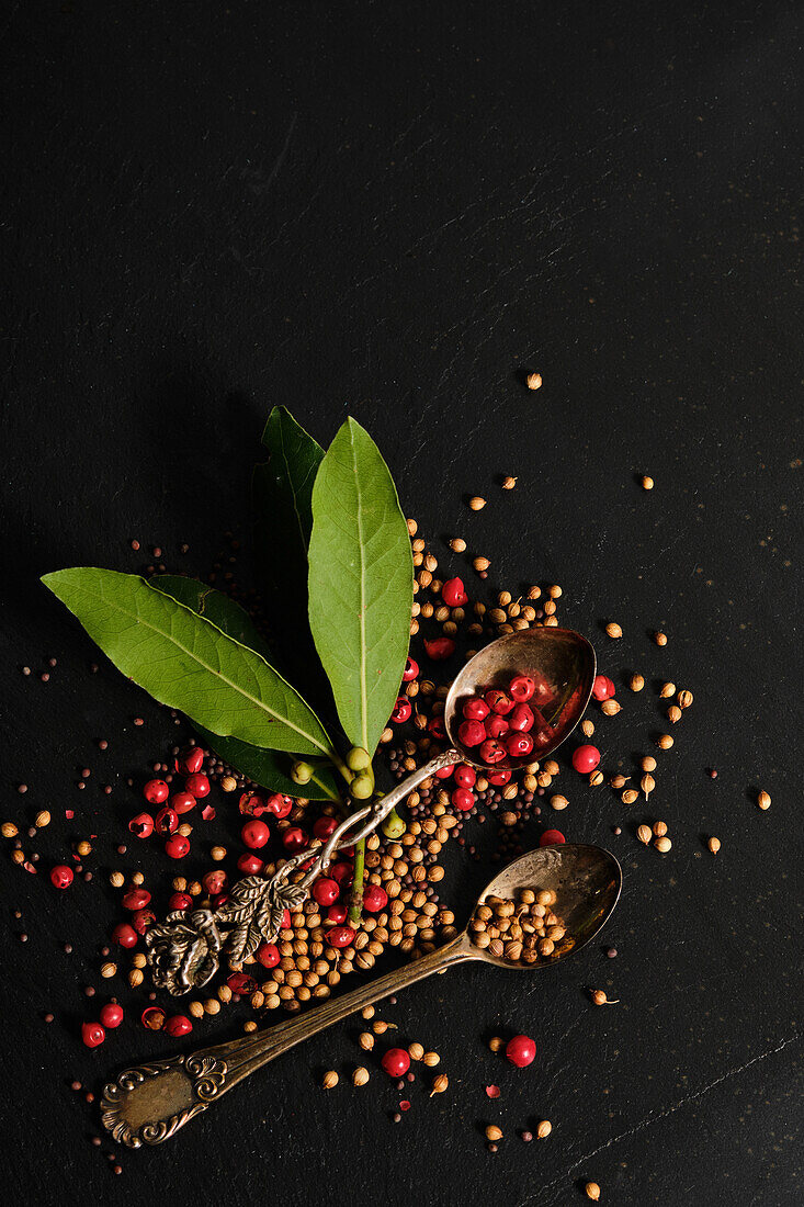 Silver spoon with pink peppercorns and coriander next to bay leaves