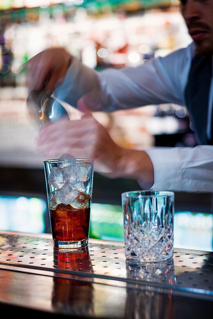 Bartender putting ice cubes in a cocktail glass