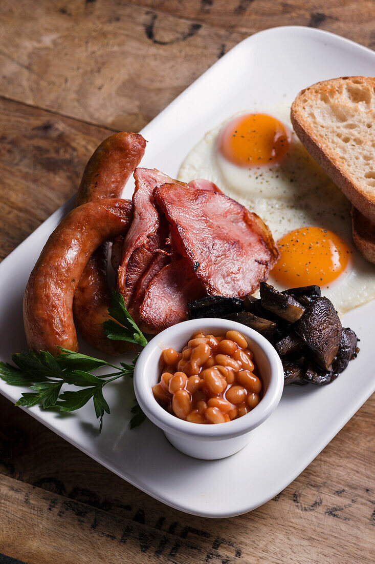 English breakfast with sausage, ham, fried egg, baked beans, mushrooms, and bread