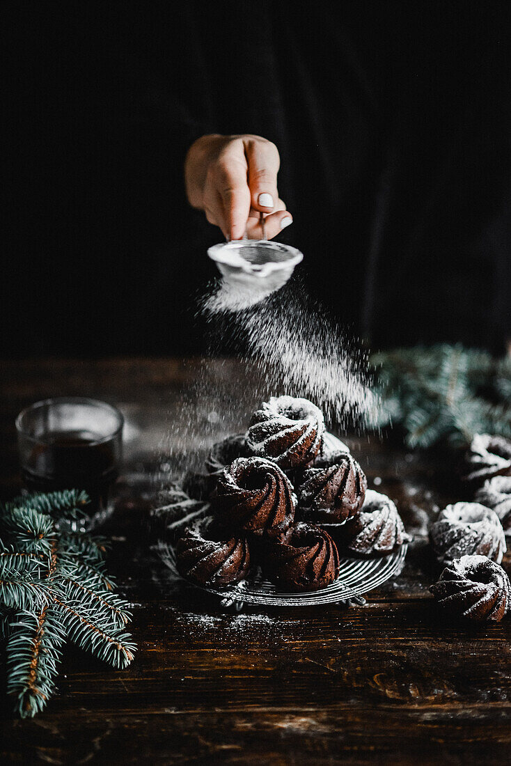 Chocolate mini bundt cakes being dusted with powdered sugar