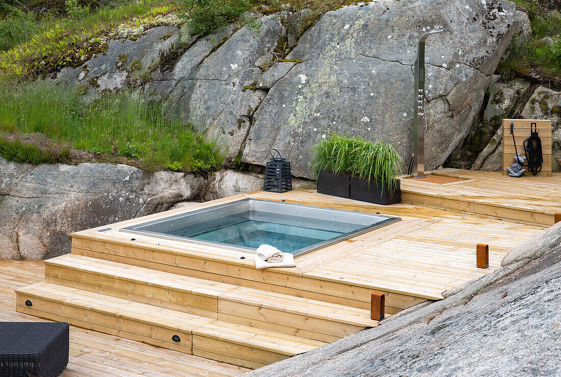 Holzterrasse mit Whirlpool und Dusche, umgeben von Felsen und Blumenbeeten