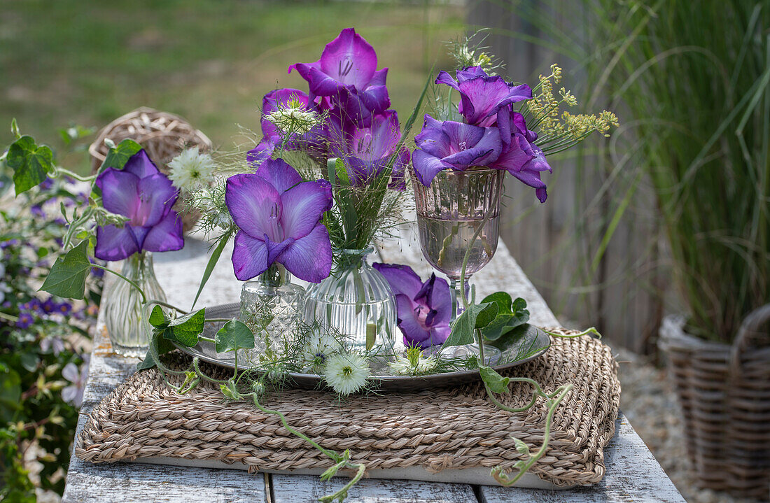 Purple gladiolus blossoms and maidenhair in glass vases on tray
