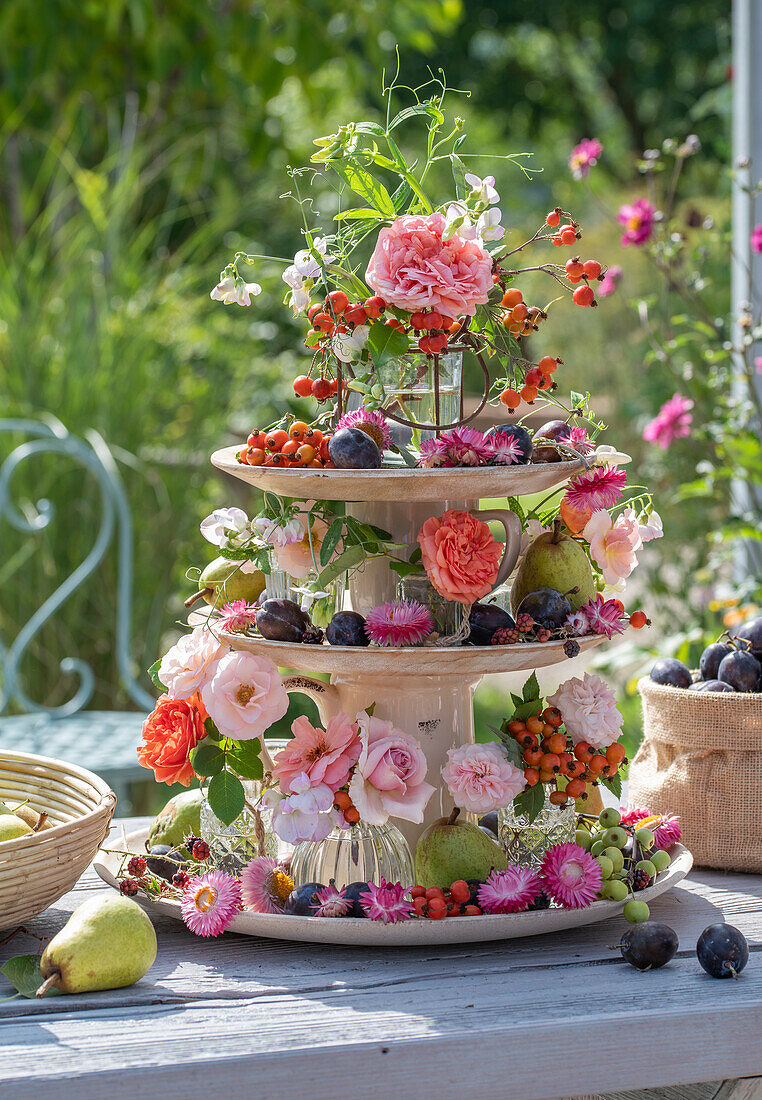 Etagere mit Rosenblüten, Strohblumen, Duftwicken, Hagebutten und Herbstfrüchten als Tischdekoration