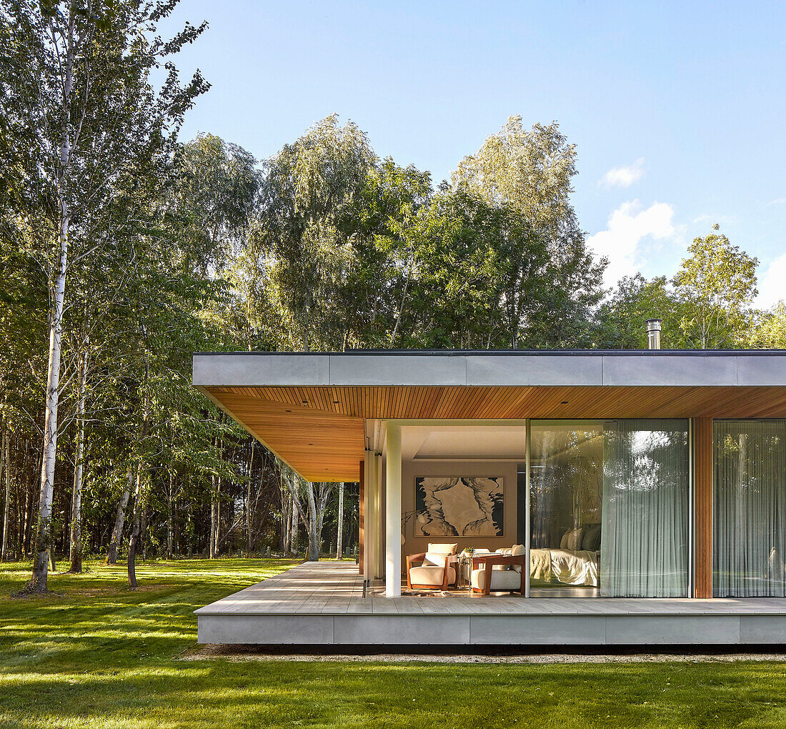 Flachdachhaus mit offenen Schiebetüren, umgeben vom Wald