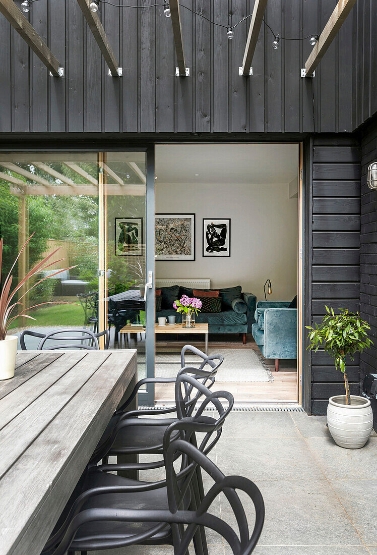 Wooden table with designer chairs on the terrace, view into the living room