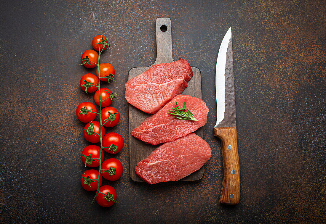 Rohe Rinderlendensteaks auf Holzbrett mit Kirschtomatenzweig